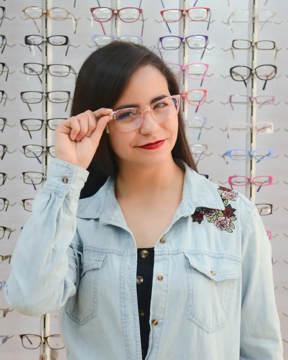 A woman trying on glasses in front of a wall of frames